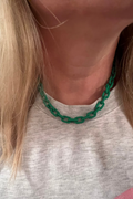 Person wearing a green chain necklace with a neutral background