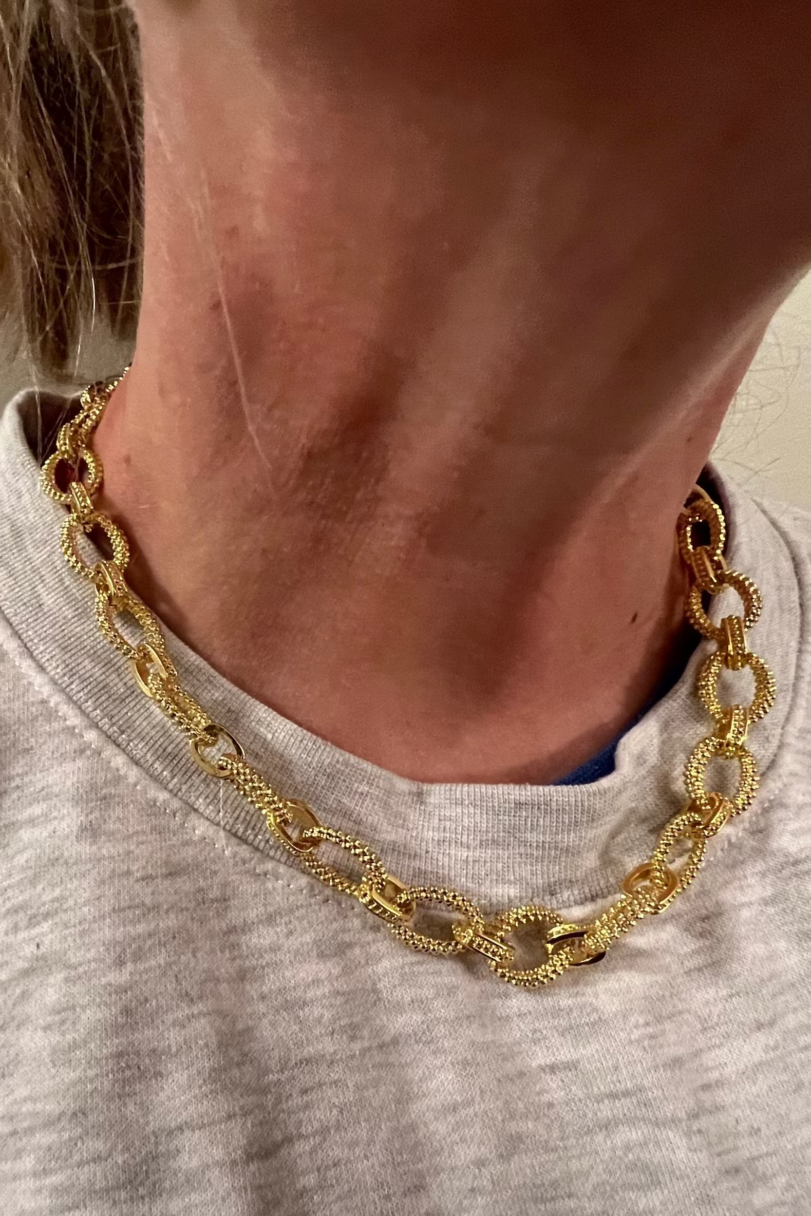 Person wearing a gold chain necklace with a neutral background