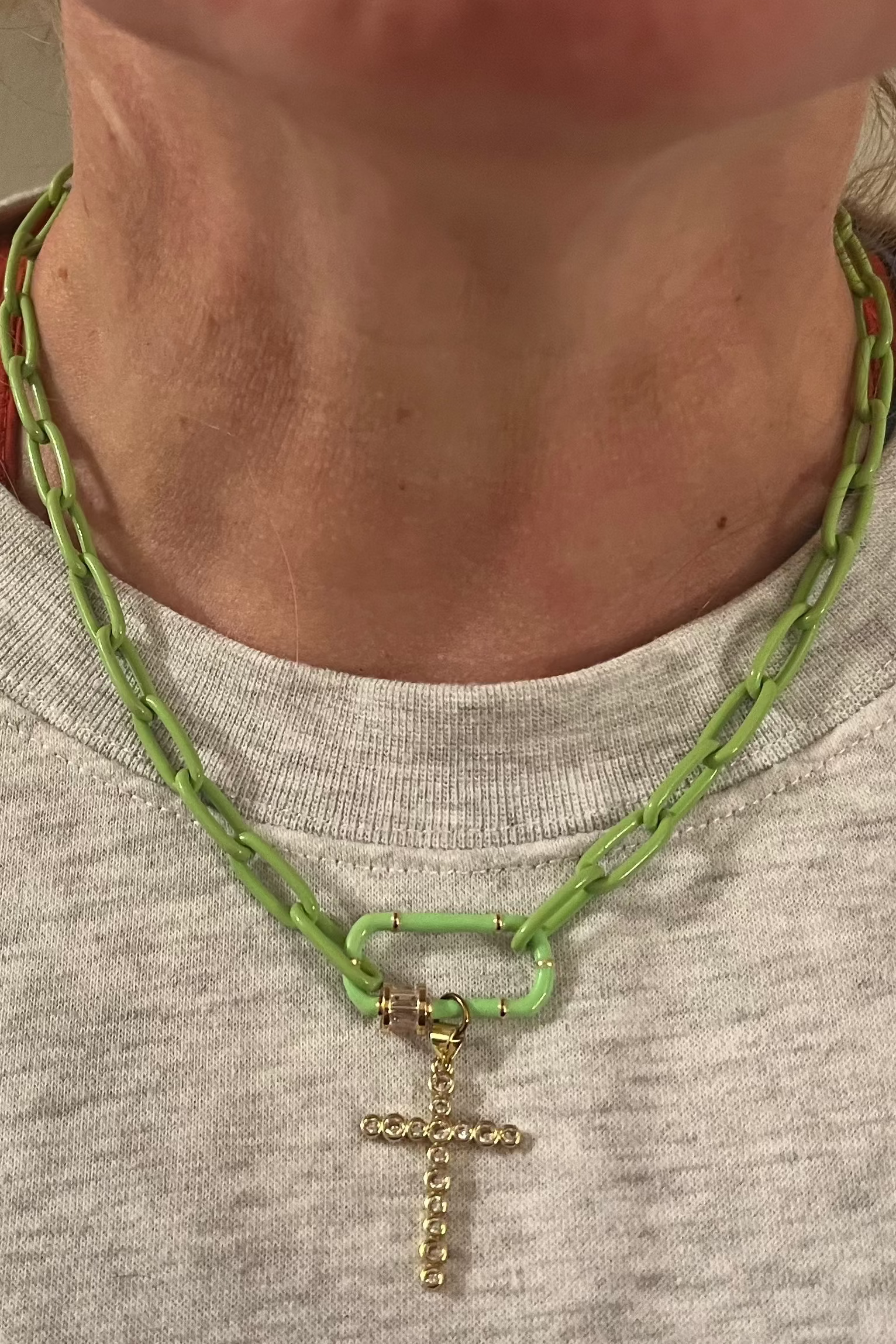 Person wearing a green chain necklace with a gold cross pendant.