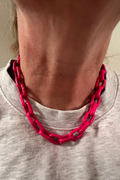 Person wearing a pink chain necklace on a plain background