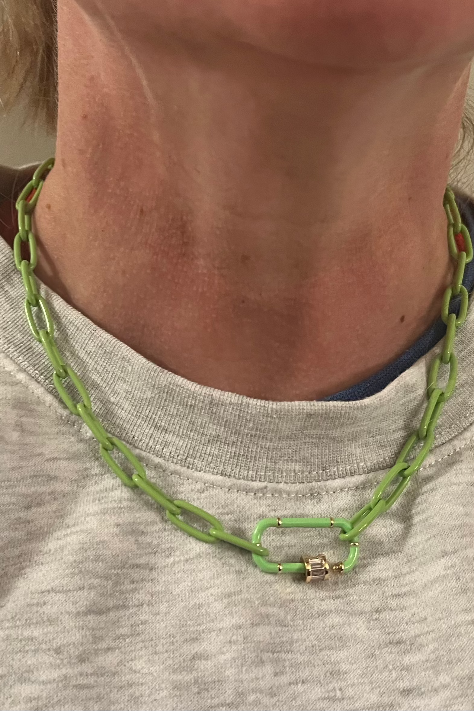 Person wearing a green chain necklace with a neutral background