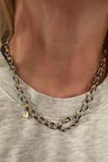 Person wearing a gold and blue chain necklace on a neutral background