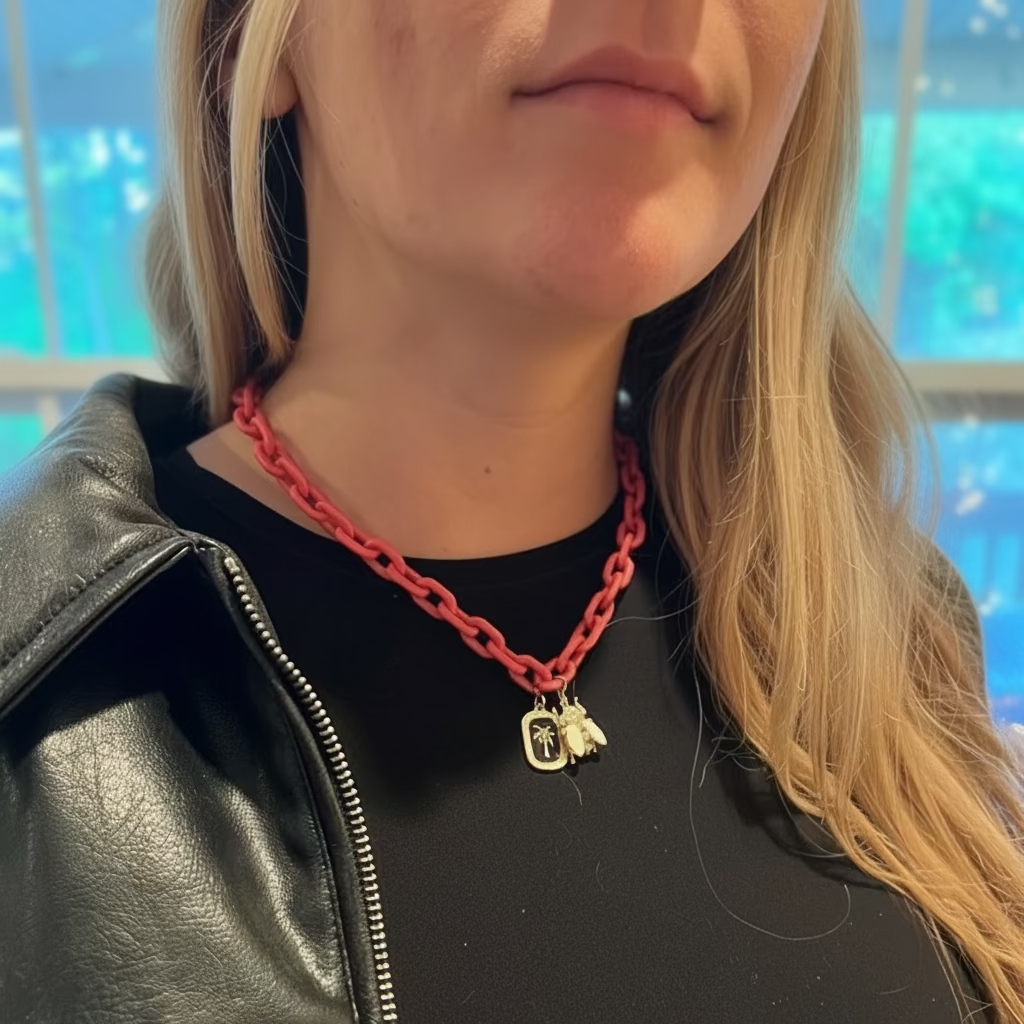 Person wearing a pink chain necklace with a bee and coconut tree pendants.